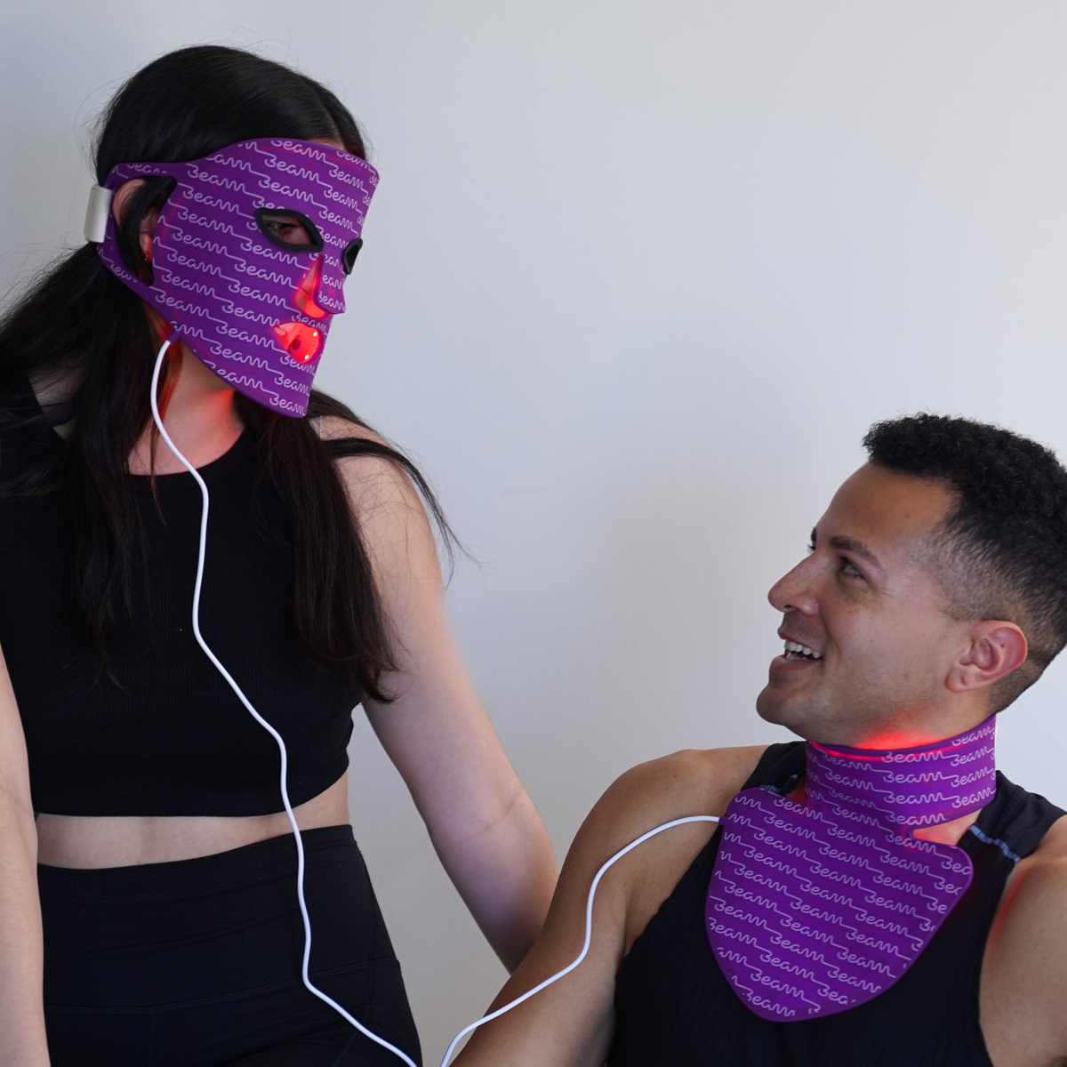 Two people demonstrating the Beam Duo face mask and neck and chest mask